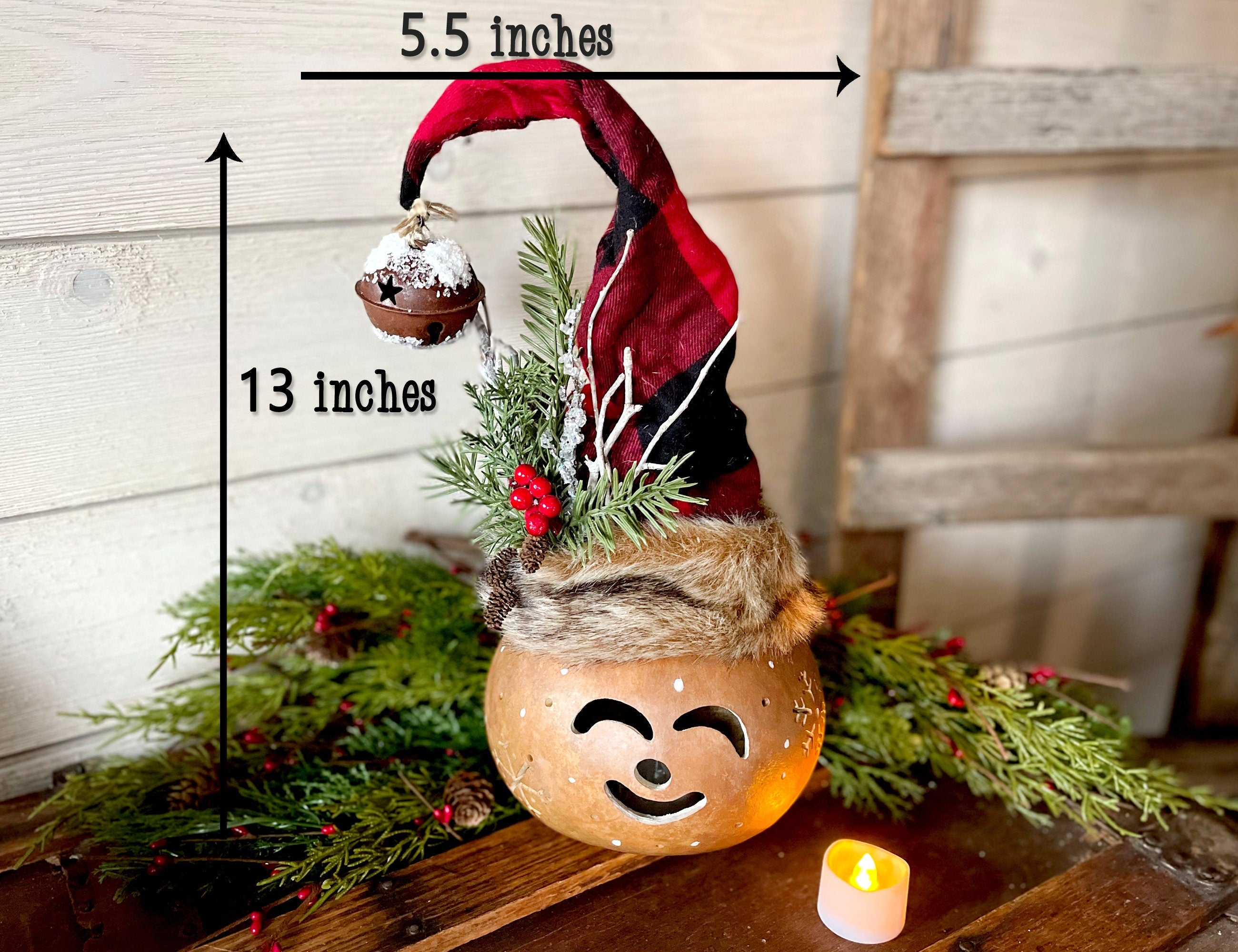 Decorative gnome with a face on a wooden surface, surrounded by greenery and a candle.