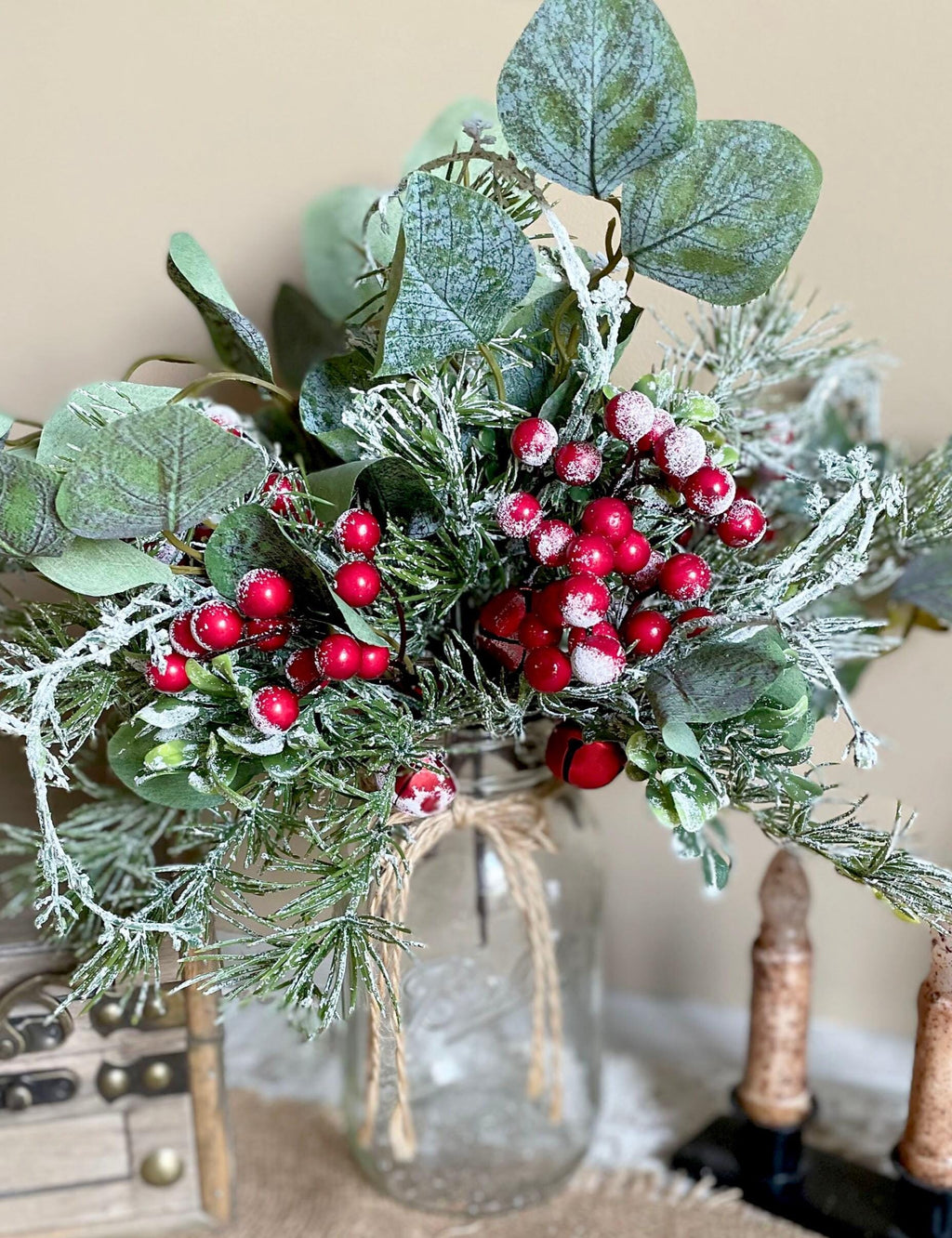 Decorative arrangement of greenery and red berries in a glass vase on a neutral background