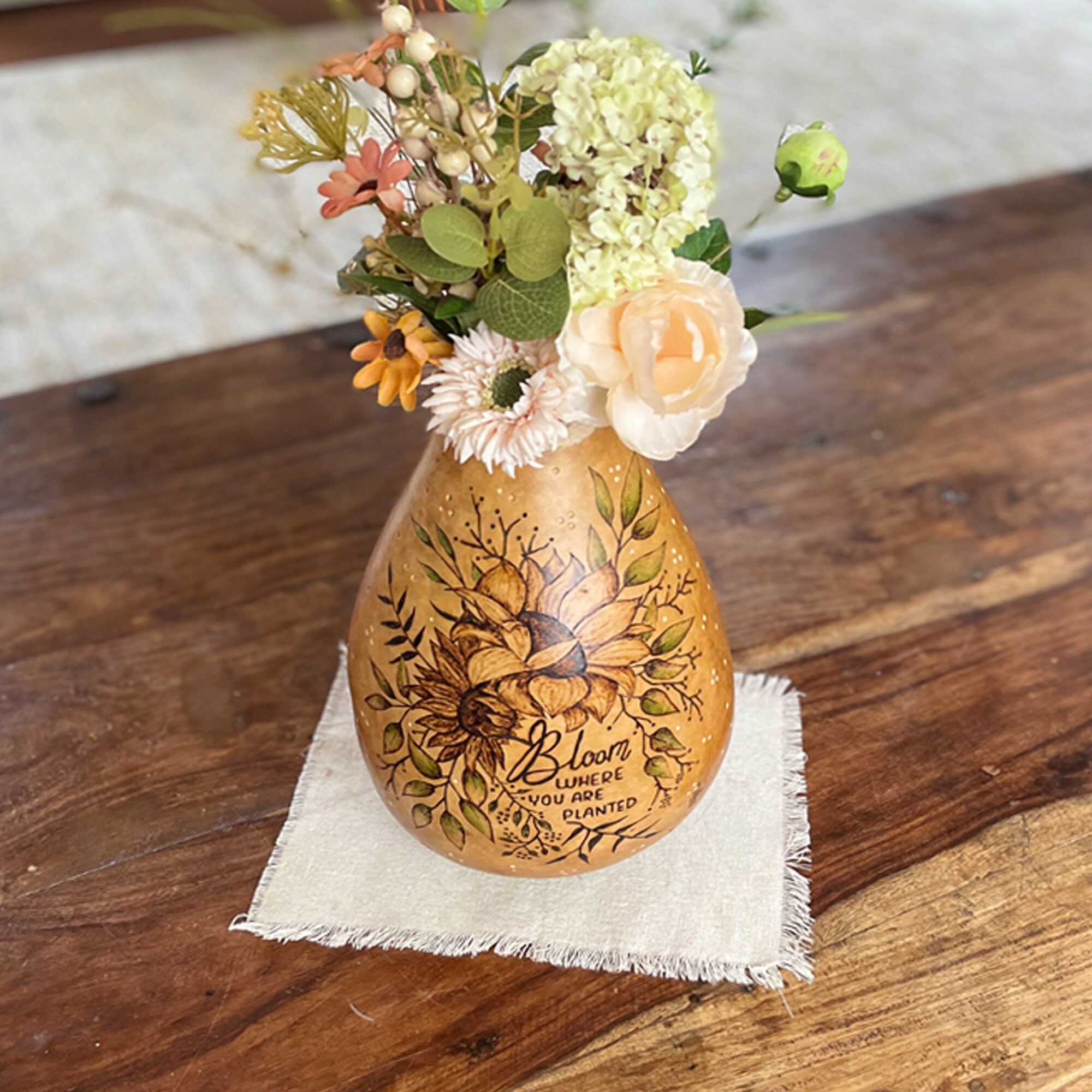 Decorative gourd vase with floral arrangement on a wooden surface