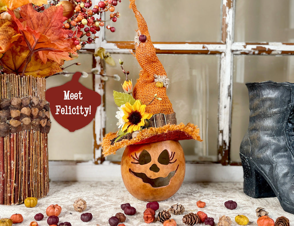 Decorative pumpkin with a witch hat and autumn leaves on a table.
