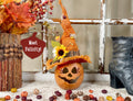Decorative pumpkin with a witch hat and autumn leaves on a table.
