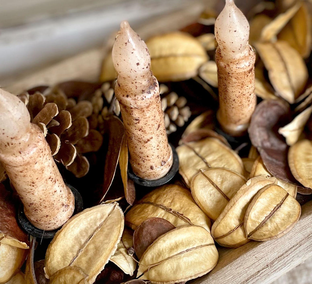 Candlesticks with textured surface on a bed of dried leaves and pinecones.