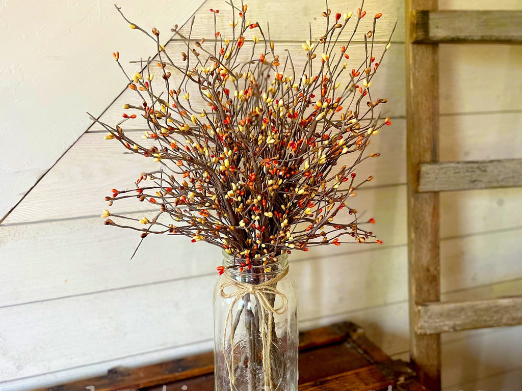 Decorative arrangement of branches with small orange berries in a clear glass jar on a wooden surface.
