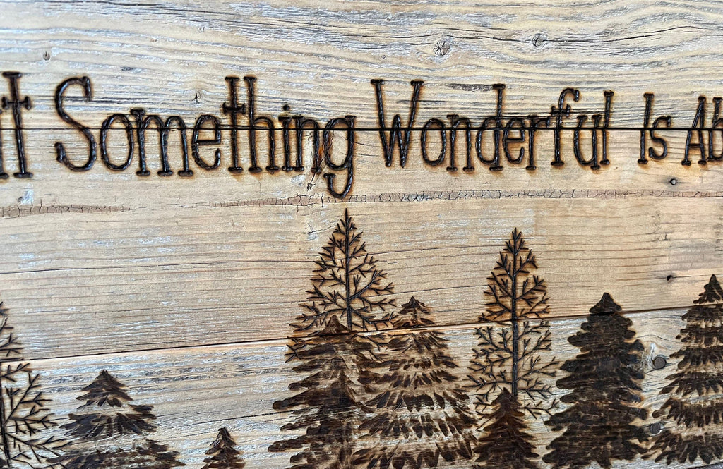 Wooden sign with engraved trees and text 'It Something Wonderful Is Ab', featuring a website address at the bottom.