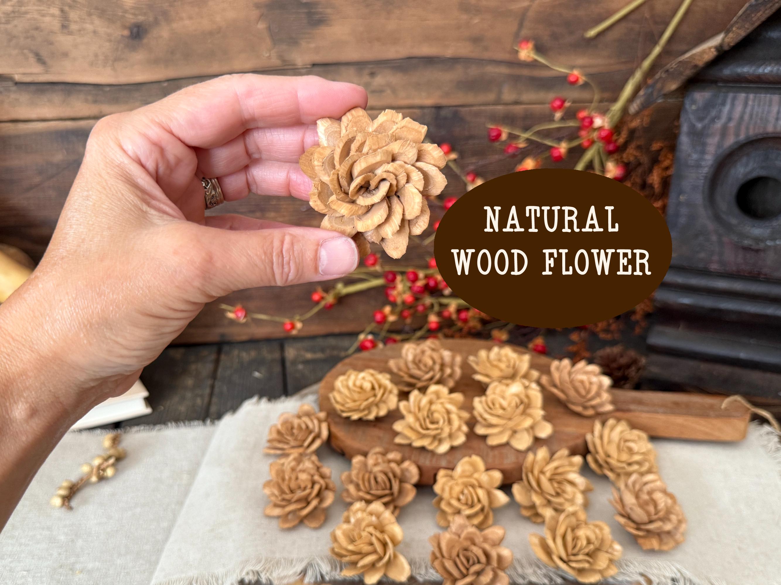 Hand holding a natural wood flower with more flowers on a rustic wooden background.