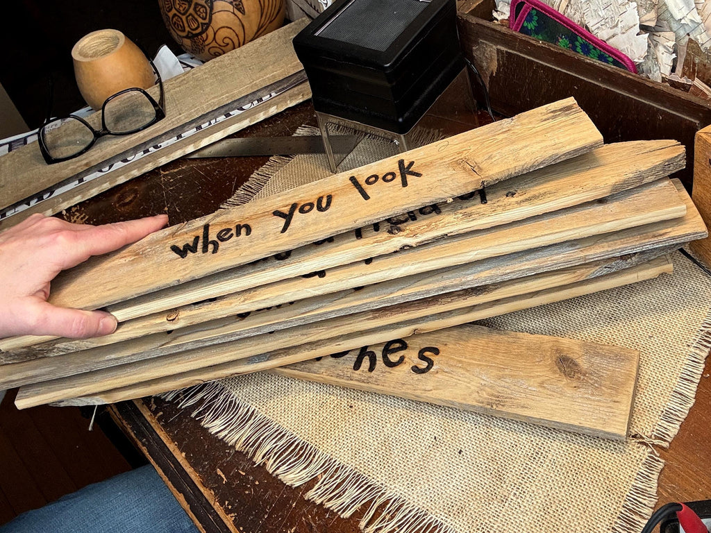 Stack of wooden planks with text on them held by a hand, placed on a textured surface.