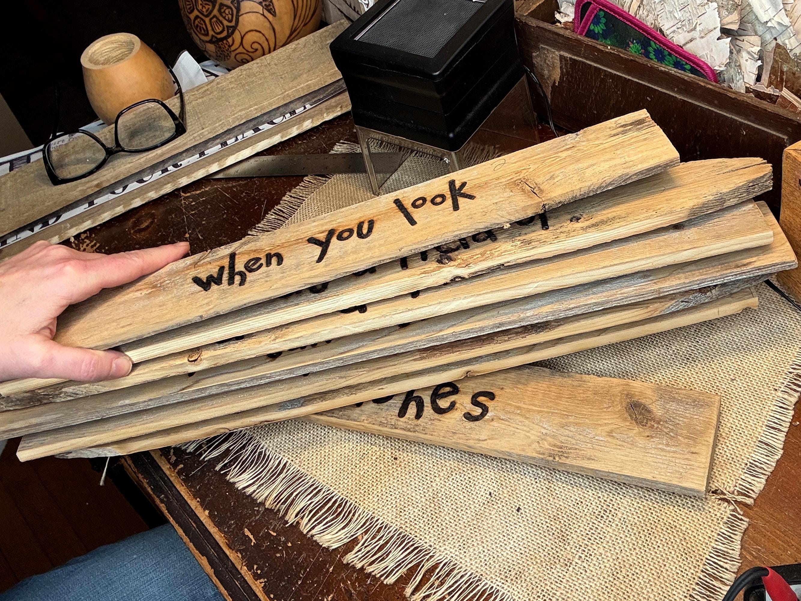 Stack of wooden planks with text on them held by a hand, placed on a textured surface.