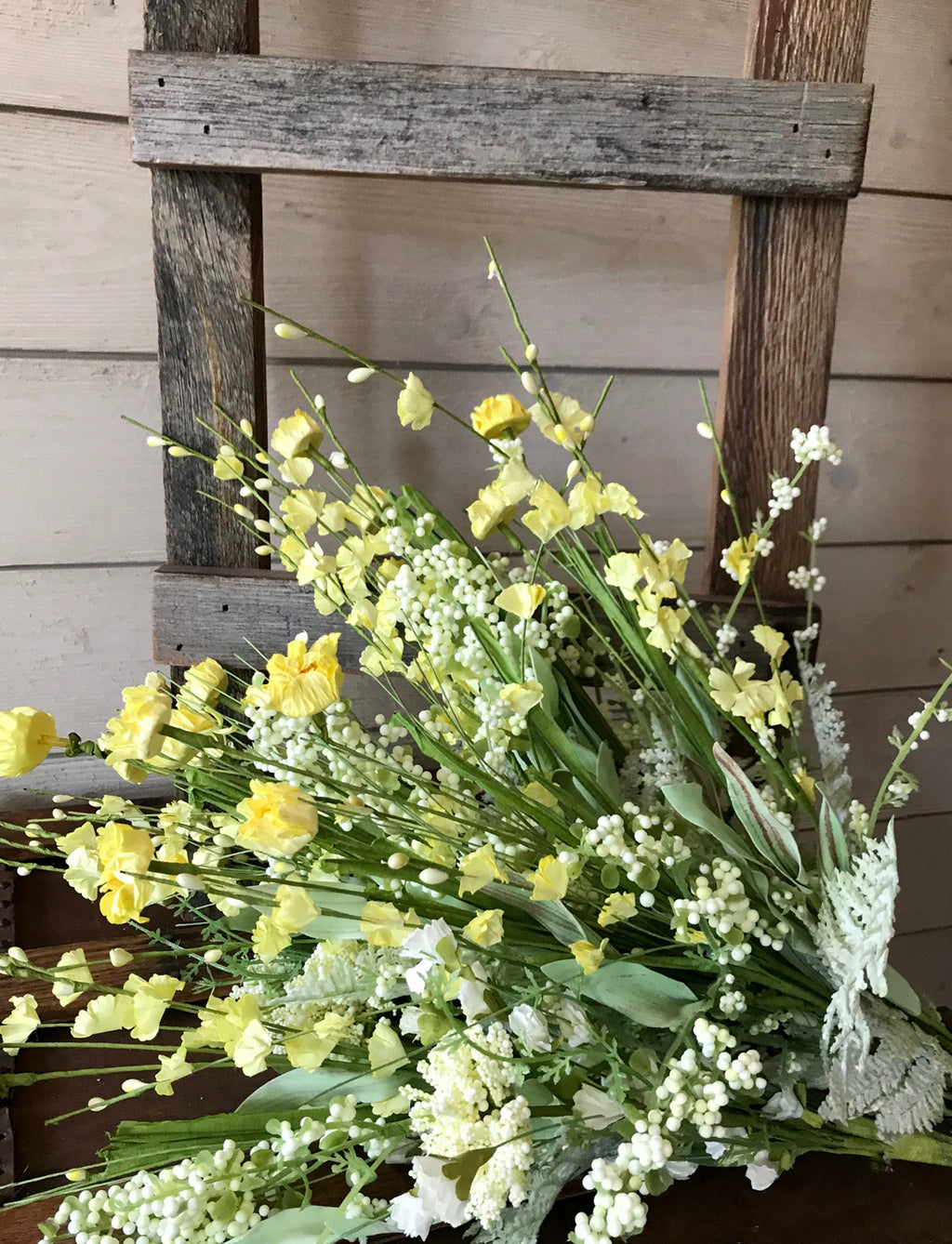 Bouquet of yellow and white flowers in front of a wooden ladder against a wooden wall.