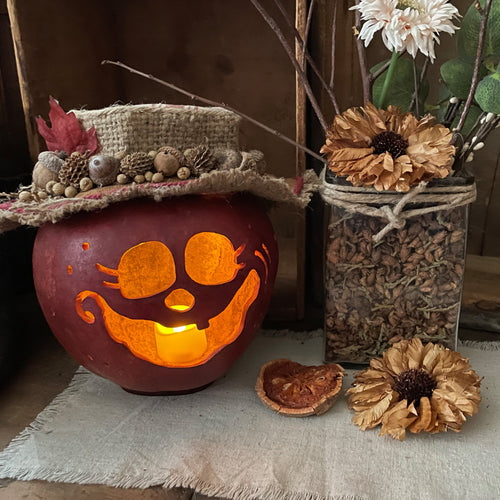 Decorative pumpkin with a carved face, surrounded by autumn-themed elements on a wooden surface.