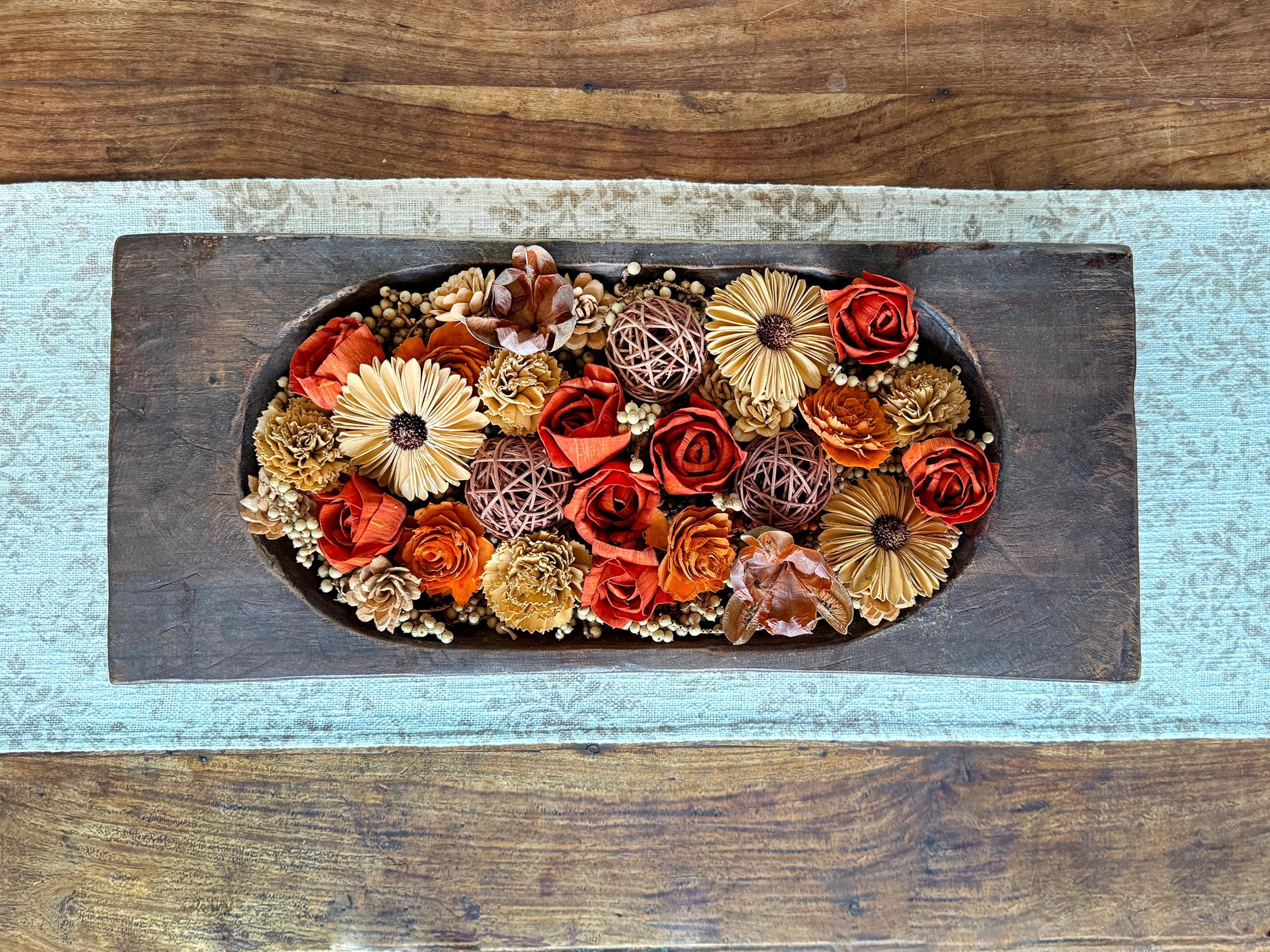 Decorative arrangement of flowers in a wooden dough bowl sitting on a coffee table.