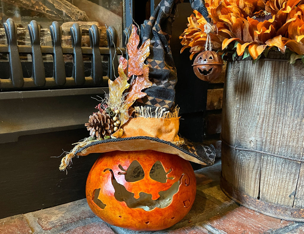 Decorative pumpkin with witch hat and carved face, placed against a rustic background.