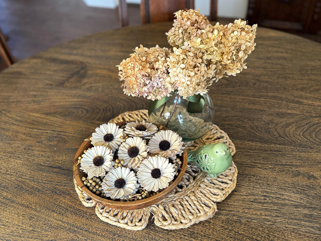 Decorative items including a vase with dried flowers, a bowl with white flowers, and a green ball on a wooden table.