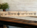 Wooden plaque with latitude and longitude coordinates on a wooden surface.