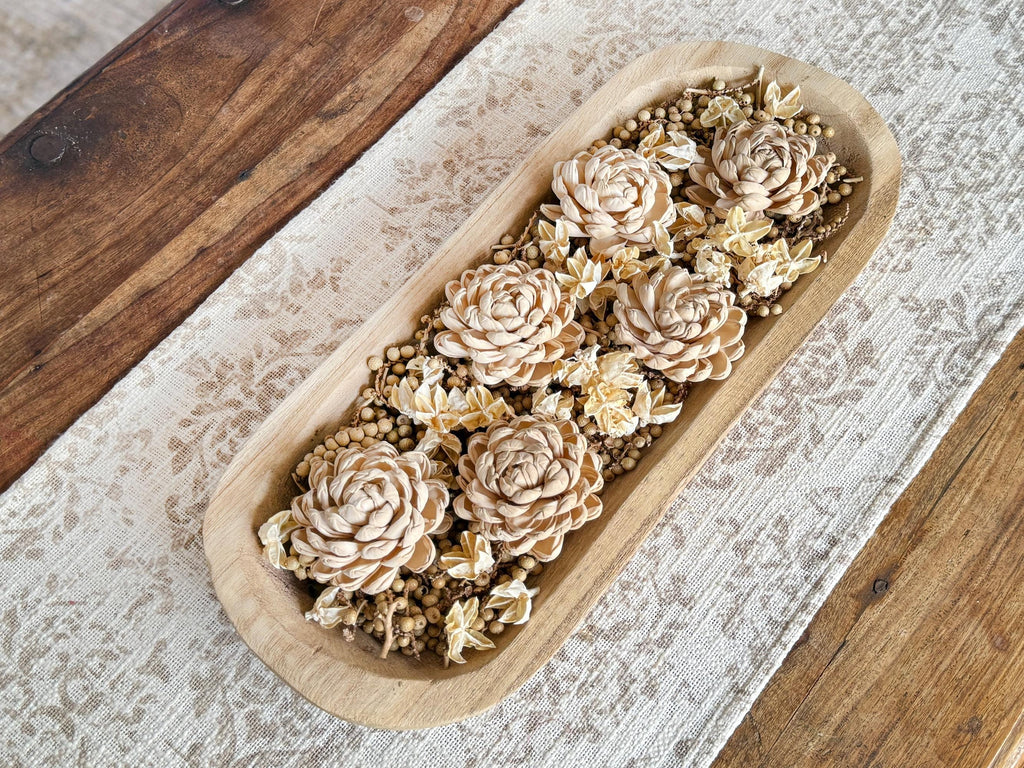 Wooden bowl filled with decorative flowers on a wooden surface