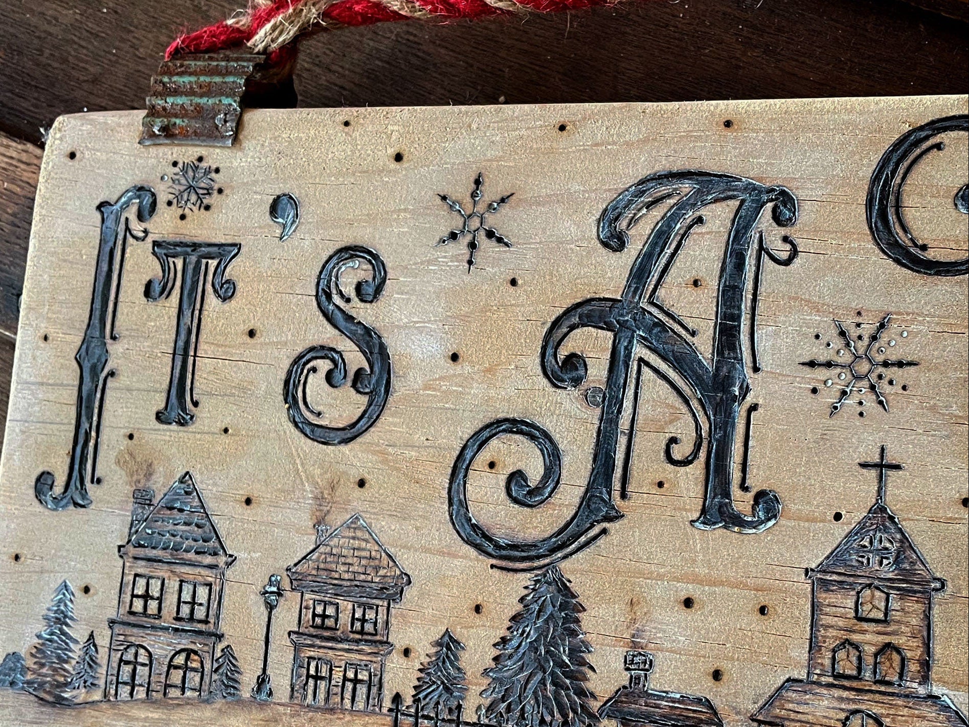 Decorative wooden sign with 'It's A' text and Christmas-themed illustrations on a rustic background.
