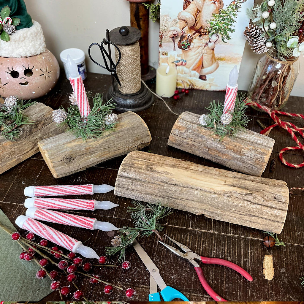 Decorative setup with wooden logs, candles, and Christmas decorations on a table.