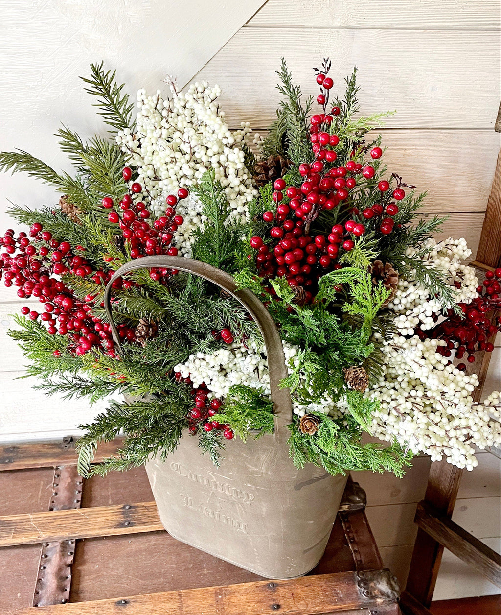 Decorative arrangement of red berries, greenery, and white flowers in a rustic basket on a wooden surface.