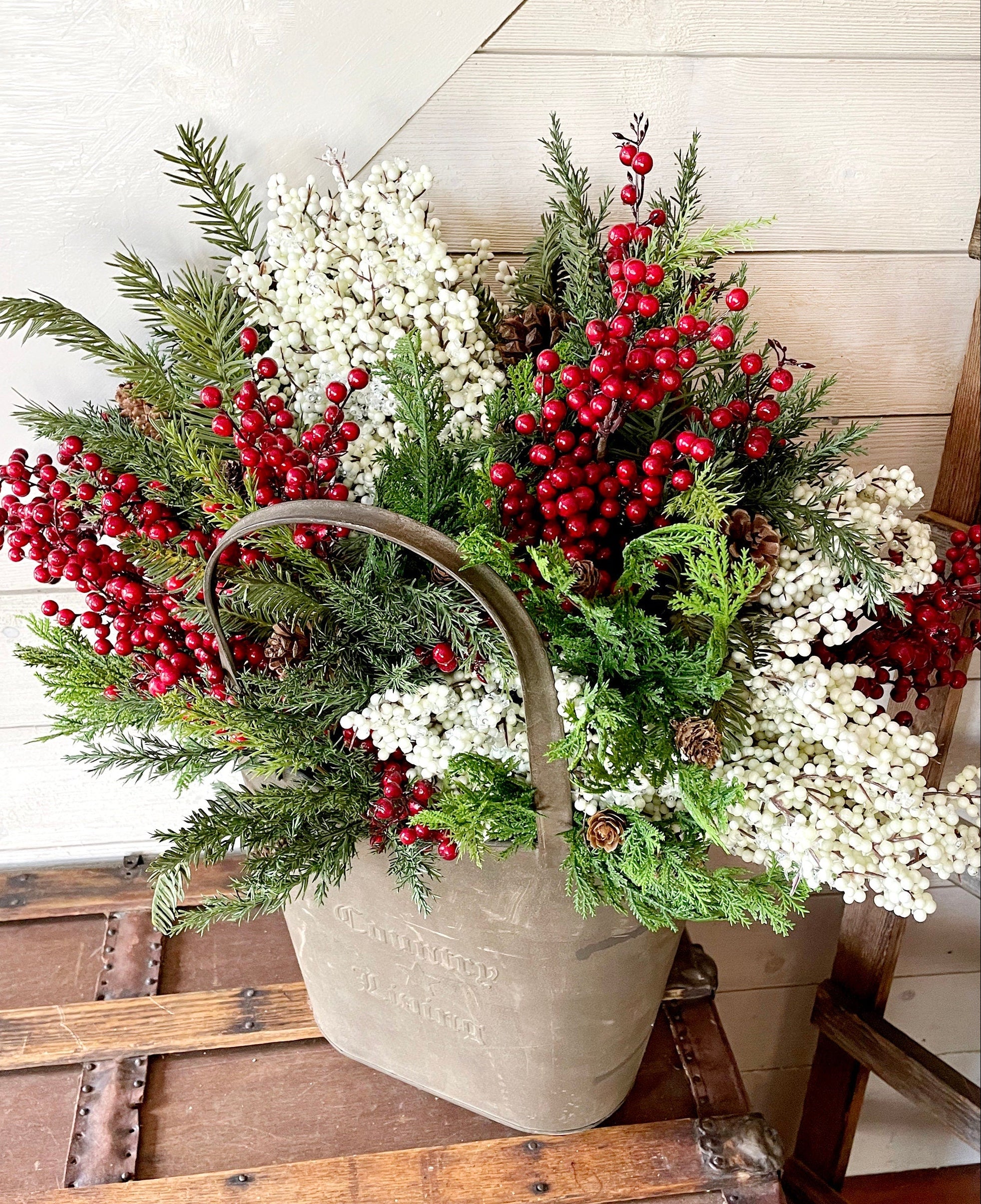 Decorative arrangement of red berries, greenery, and white flowers in a rustic basket on a wooden surface.