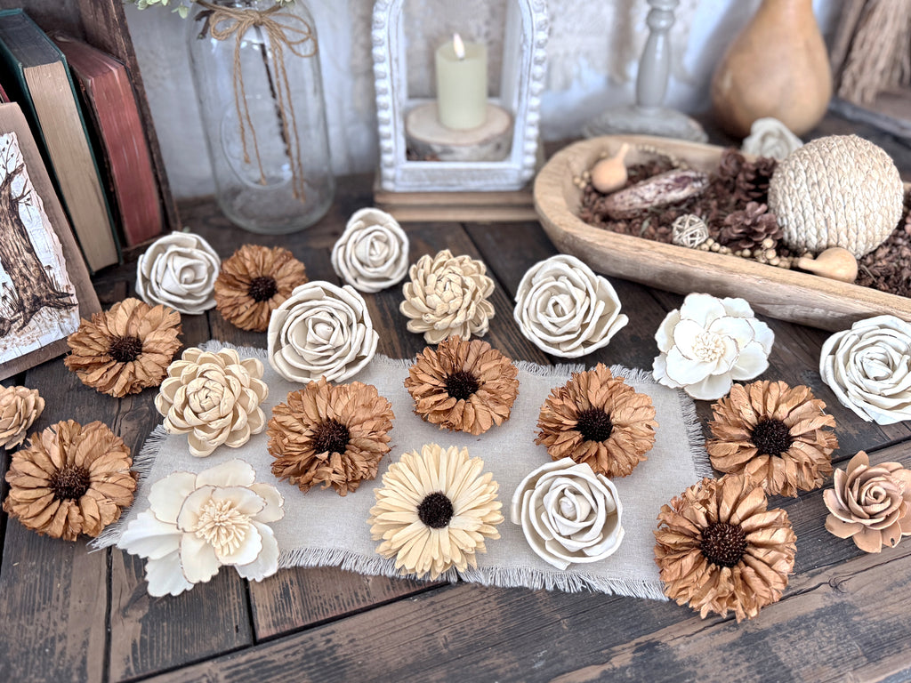 Decorative wood flower blossoms in beige and spicey yellow on a wooden surface with a candle and books in the background.