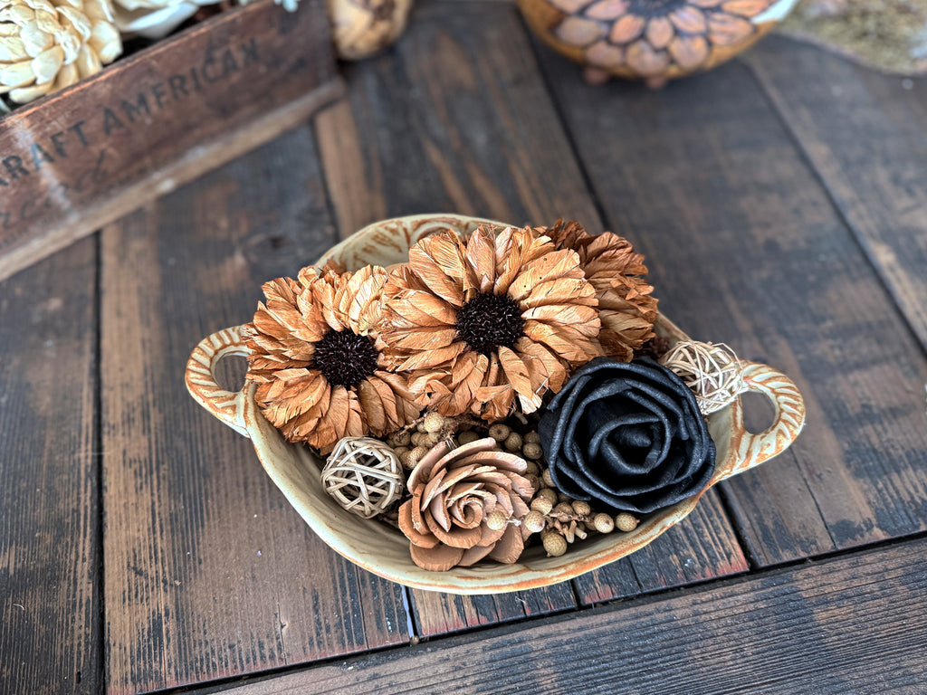 Decorative bowl with wood flower blossoms  in black and brown. Bowl sits on a wooden surface