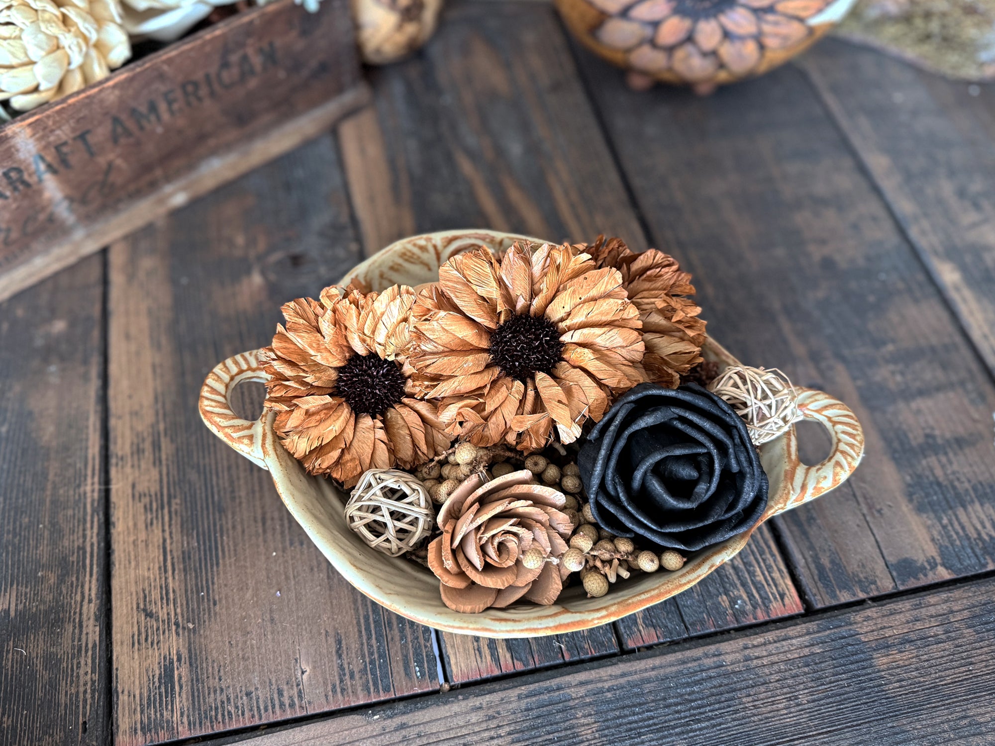 Decorative bowl with wood flower blossoms  in black and brown. Bowl sits on a wooden surface