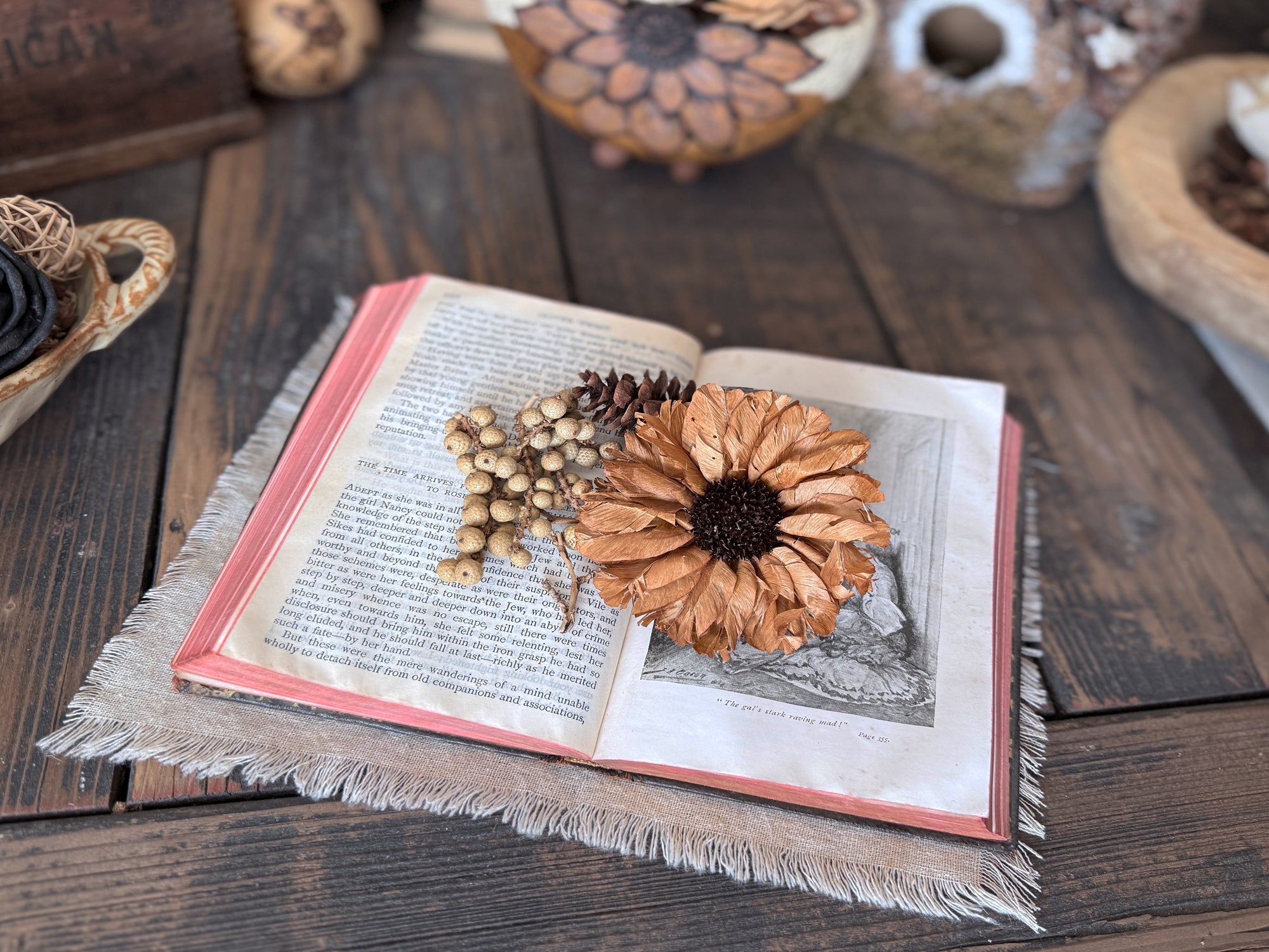Open book with dried flower blossom and pinecones on a wooden surface