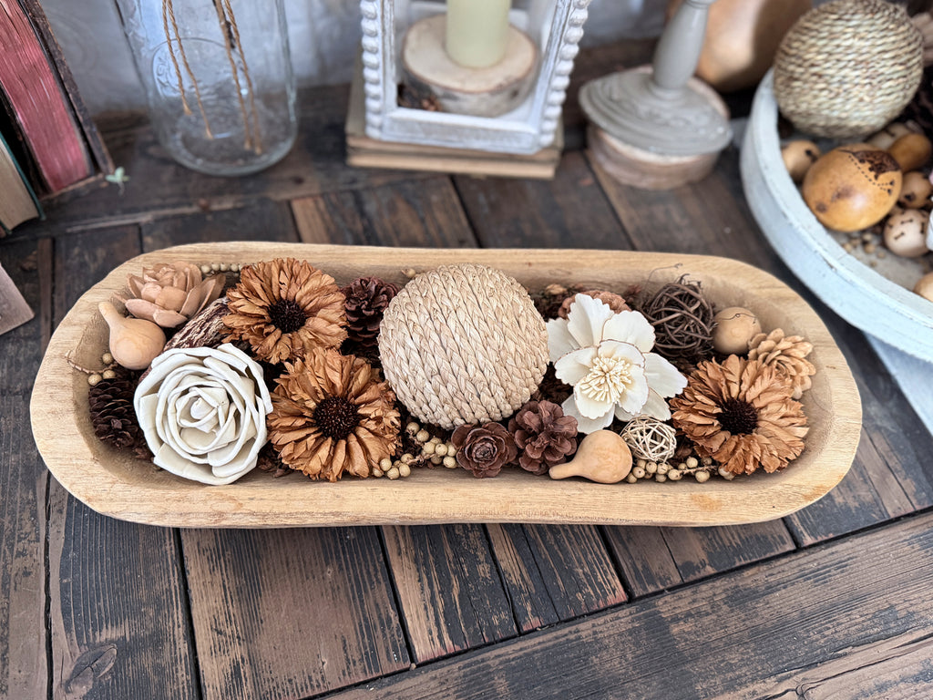 Decorative wooden dough bowl arrangement of flowers and pinecones in a wooden bowl on a wooden surface.