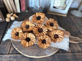 Decorative arrangement of natural wood flower blossoms on a wooden surface with books and a candle in the background.