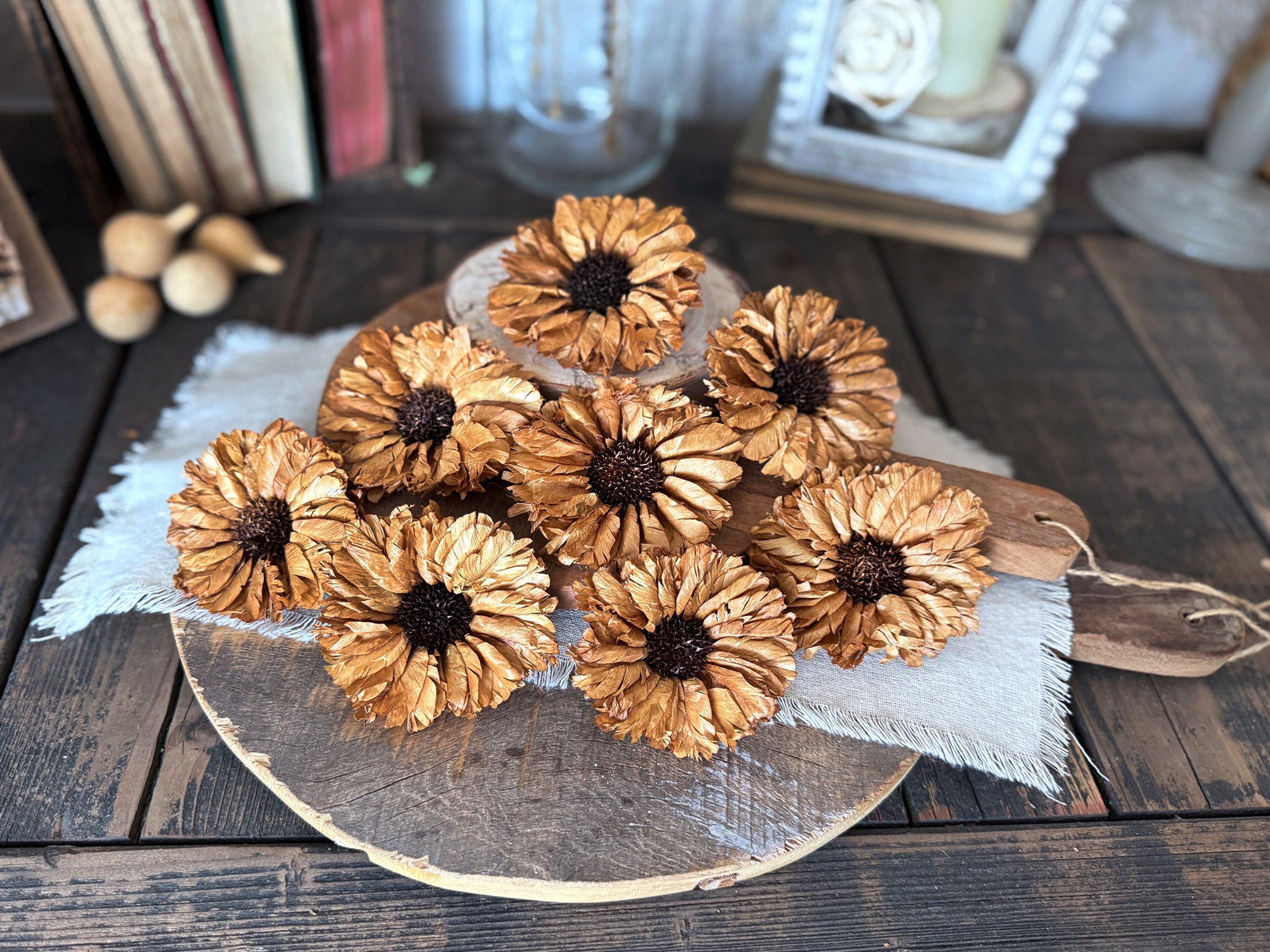 Decorative arrangement of natural wood flower blossoms on a wooden surface with books and a candle in the background.