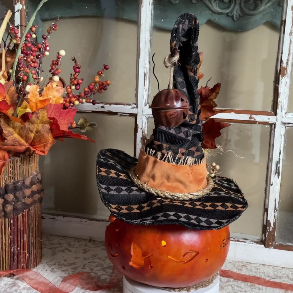 a hand carved pumpkin gourd with a black witch hat.