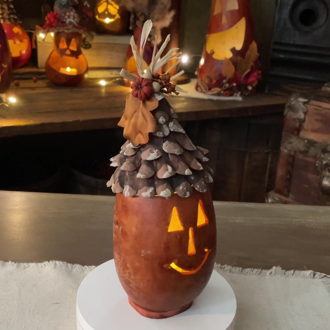 A carved gourd made into a fall pumpkin. Top is decorated with pine cone pieces.