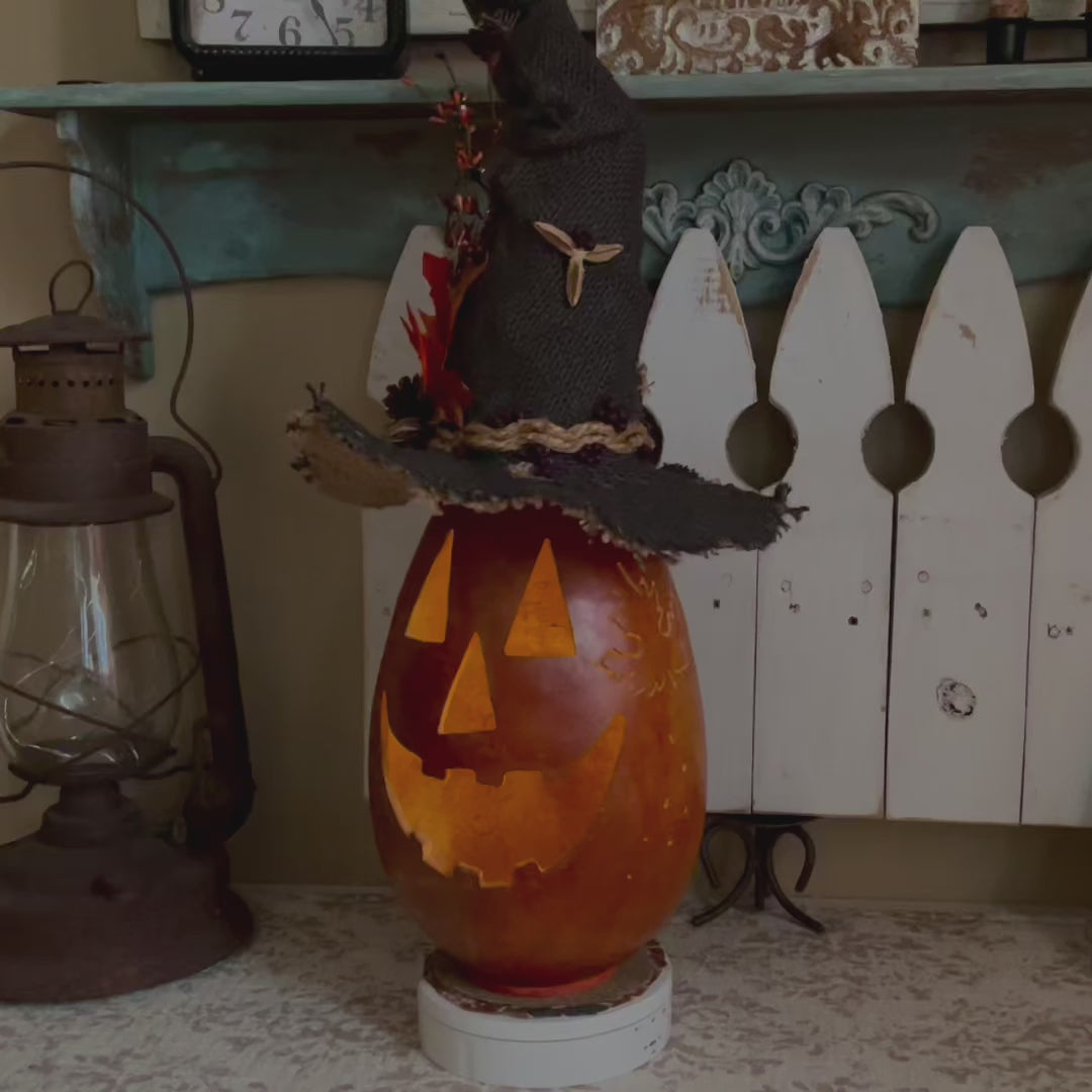 a carved pumpkin gourd with a handmade black burlap witch hat. 